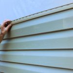 An experienced contractor installs vinyl siding plastic panels on facade wall of new home