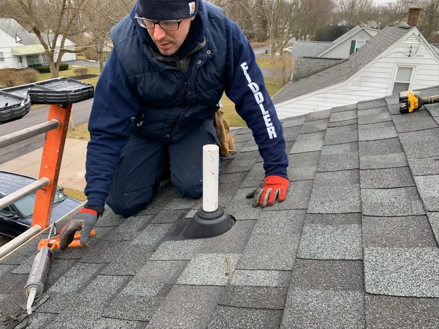 Homeowner using a snow rake to clear shingle roof, showing winter maintenance to extend your roof’s life