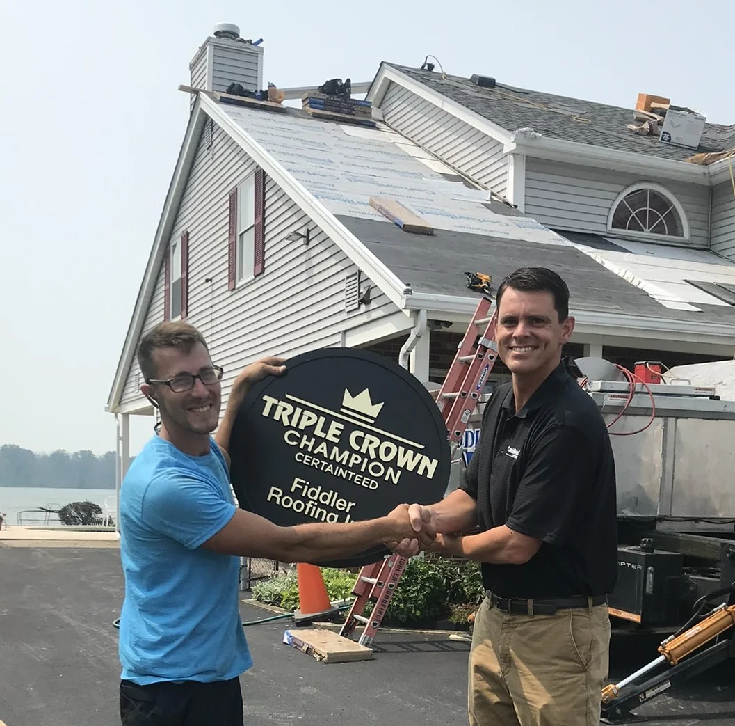 Fiddler Roofing team celebrating cleanup excellence award—employees in branded attire holding award certificate, smiling proudly in front of pristine job site and branded vehicle after another family-safe roof installation.